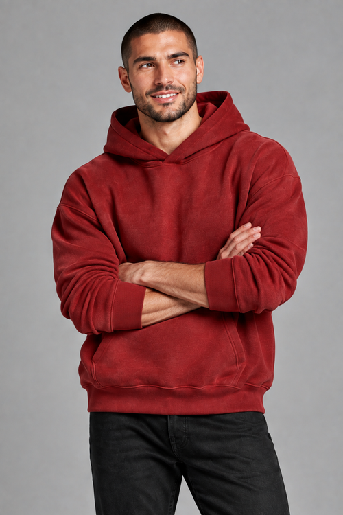 Close-up of the buzz-cut male model with arms loosely crossed, wearing the deep red hoodie on the gray backdrop