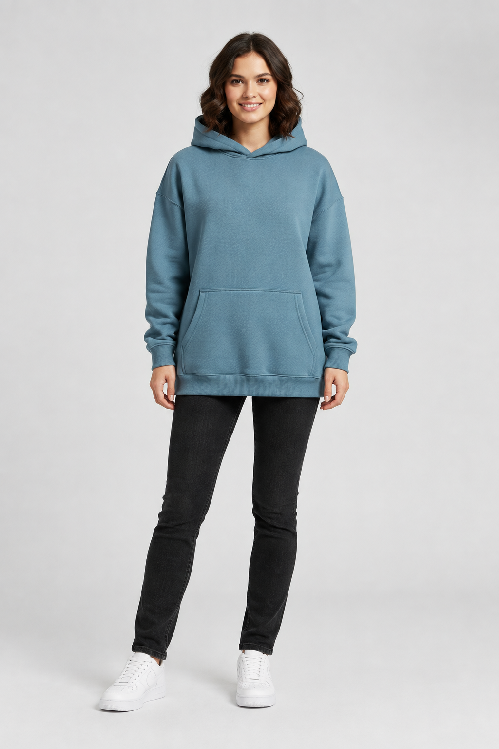 Full-body brunette female model wearing the slate-blue hoodie and black jeans