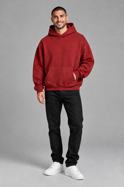 Full-body studio shot of a smiling male model with a buzz cut, in the deep red hoodie on the gray backdrop