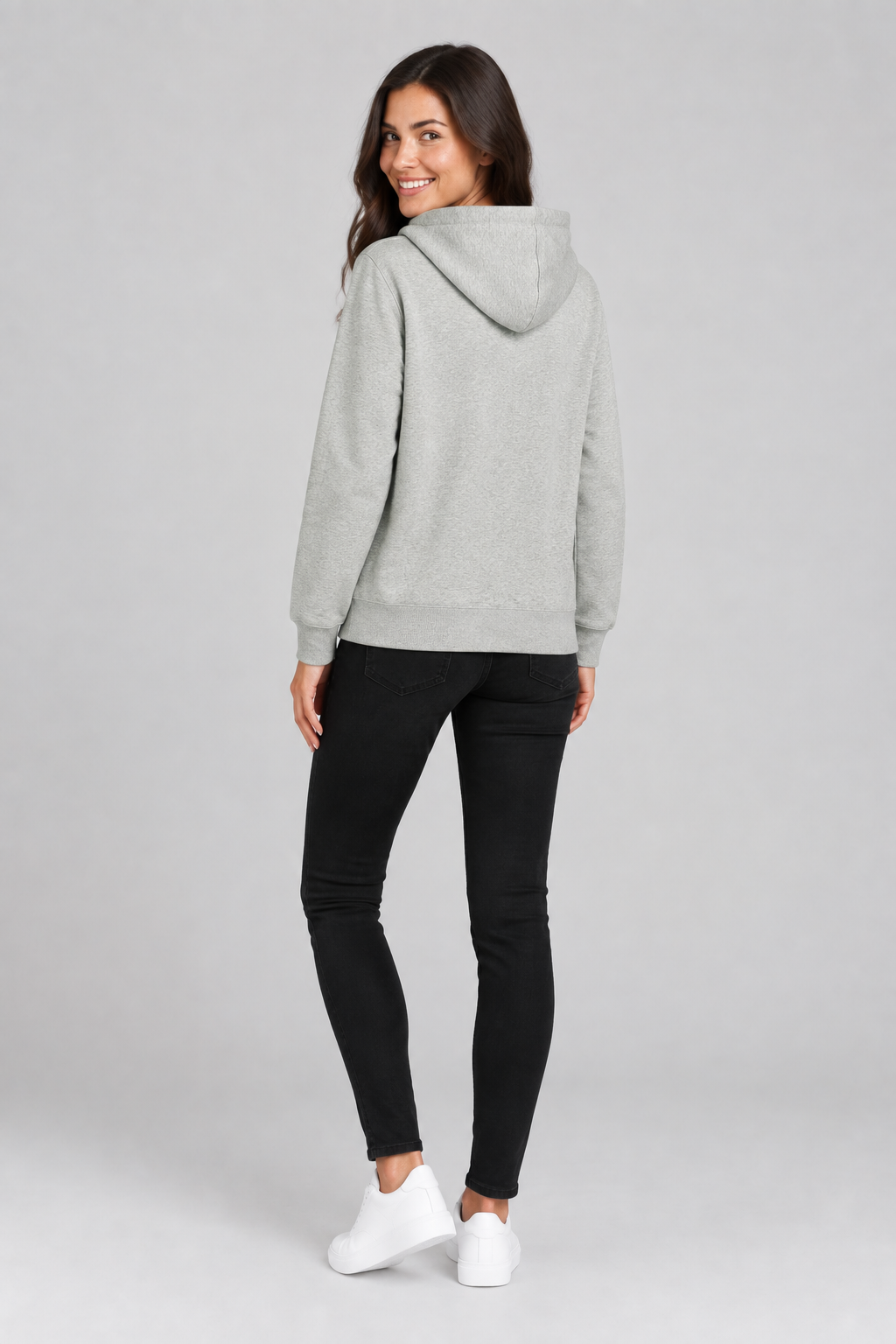 Rear studio view of the brunette model wearing the hoodie and looking back at the camera